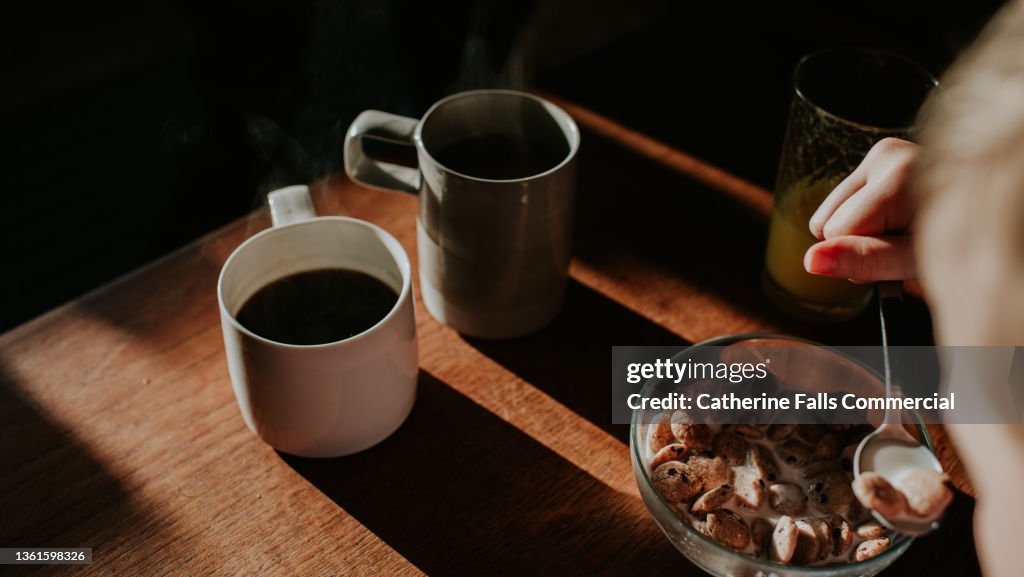 Two cups of coffee on a wooden table with a bowl of breakfast cereal