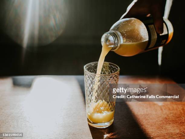 a hand pours a plastic bottle of fresh orange juice into a glass - orangensaft stock-fotos und bilder