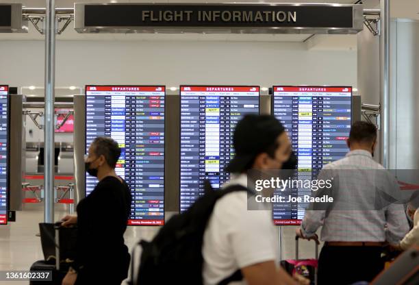 Travelers pass the flight information board as they make their way through Miami International Airport on December 28, 2021 in Miami, Florida. Over...