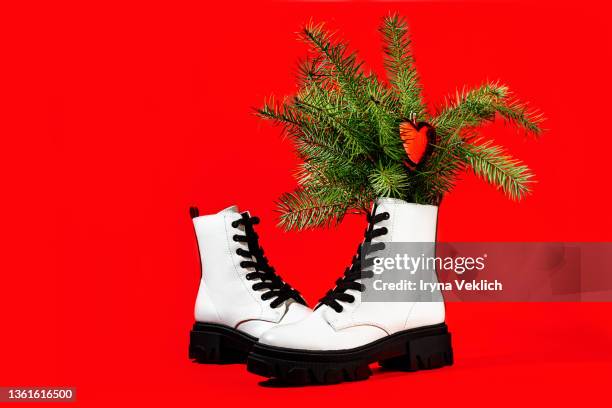 trendy fashion concept made of white color boots shoes with branches of a christmas tree with red heart toy on red color background. - black lace background stock pictures, royalty-free photos & images