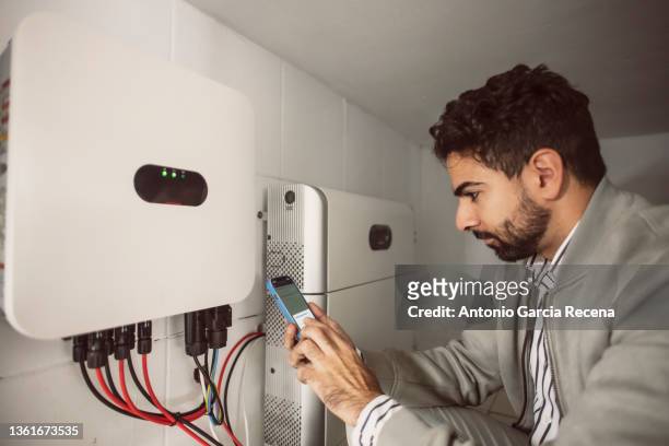 commercial agent and technical electrician synchronize the converter and the storage battery of the solar panels through the mobile phone application - india phone professional stock-fotos und bilder