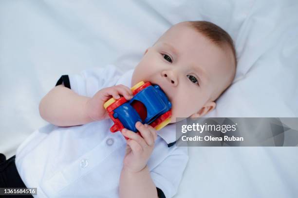 curious baby biting toy car lying down on back. - baby eating toy foto e immagini stock