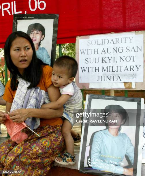 Myanmarese woman knits as she sits with a child by railings adorned with placards and pictures of democratic leader Aung San Suu Kyi during a protest...