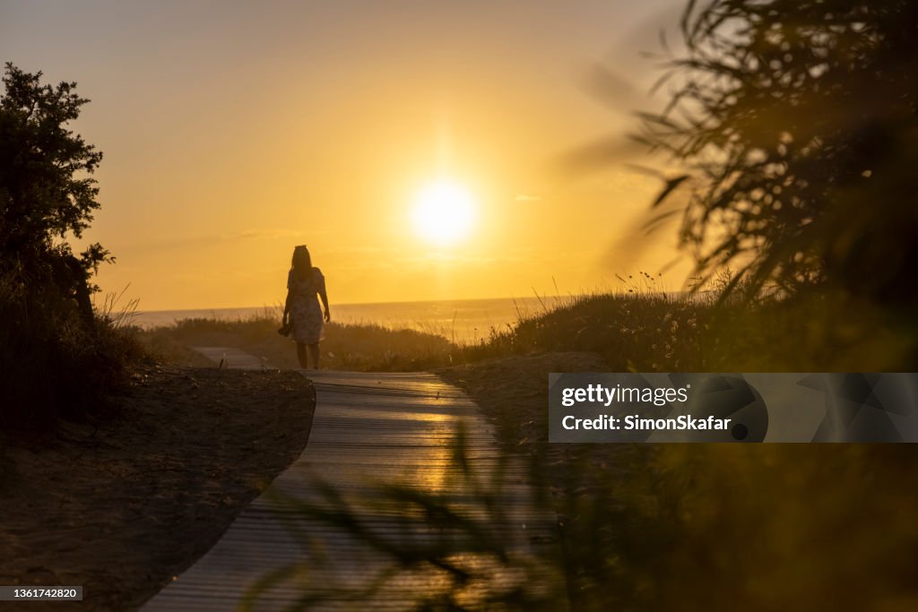 Femme en robe d’été partant sur un chemin de plage en été au coucher du soleil, Sardaigne, Italie.