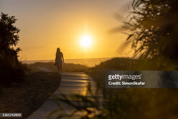 woman with summer dress leaving on a beach path in summertime at sunset, sardinia, italy. - end of summer stock pictures, royalty-free photos & images