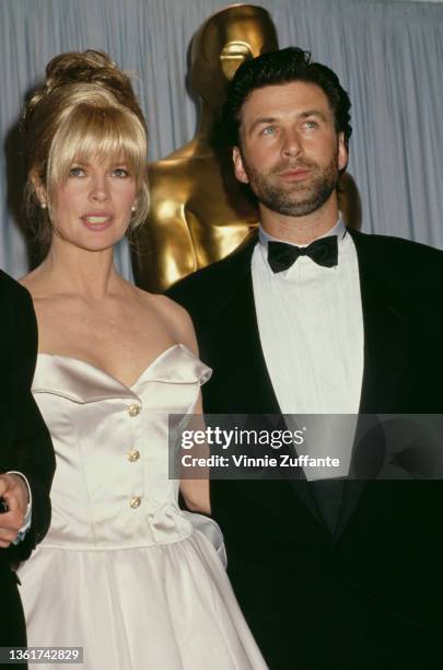American actress Kim Basinger, wearing a white strapless evening gown, and American actor Alec Baldwin, wearing a tuxedo and bow tie, attend the 63rd...