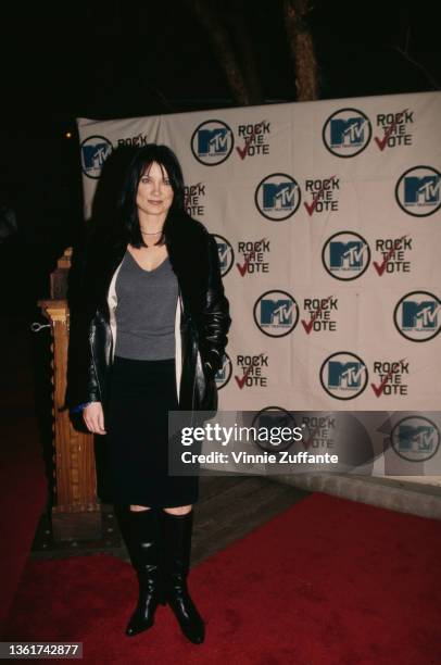 American singer-songwriter and guitarist Meredith Brooks, wearing a grey sweater beneath a black leather jacket with a black skirt and black boots,...