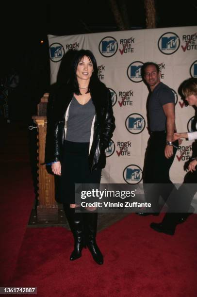 American singer-songwriter and guitarist Meredith Brooks, wearing a grey sweater beneath a black leather jacket with a black skirt and black boots,...