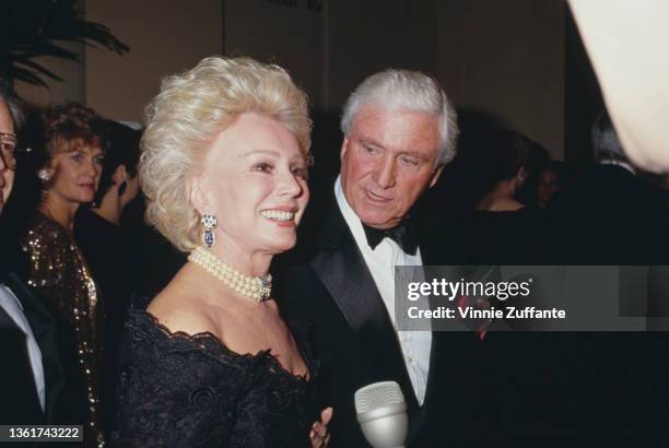 Hungarian-American actress and socialite Eva Gabor , wearing a black off-shoulder dress with a pearl choker, and American television host Merv...