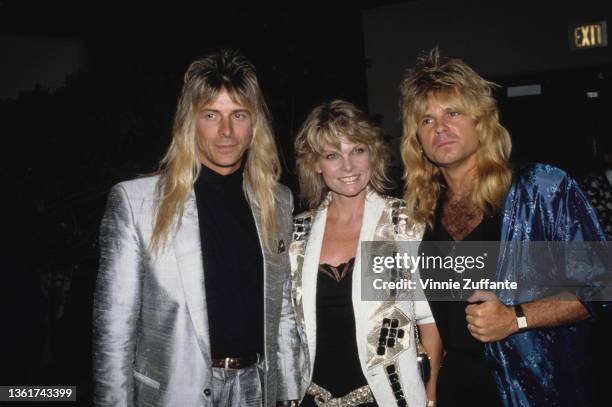 American keyboard player Gregg Giuffria wearing a silver suit jacket over a black shirt, American actress Cathy Lee Crosby, wearing a white jacket...