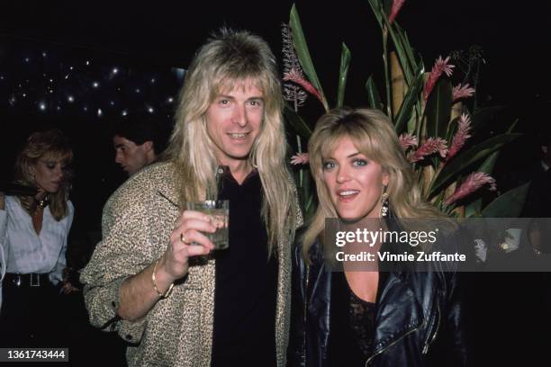 American keyboard player Gregg Giuffria holding a glass as he stands beside American actress Lydia Cornell, wearing a black leather jacket, at an...