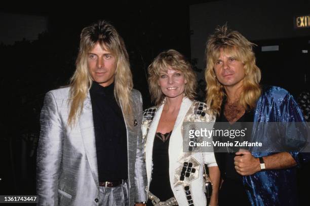 American keyboard player Gregg Giuffria wearing a silver suit jacket over a black shirt, American actress Cathy Lee Crosby, wearing a white jacket...