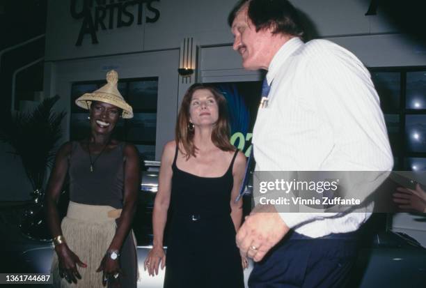 Jamaican-American fashion model, singer and actress Grace Jones, wearing a gold-fringed outfit with an Asian-style conical hat, American actress Lois...