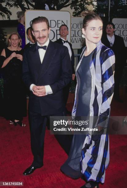 British actor Ralph Fiennes, wearing a tuxedo and bow tie, and his partner, British actress Francesca Annis, wearing a blue, black and grey striped...