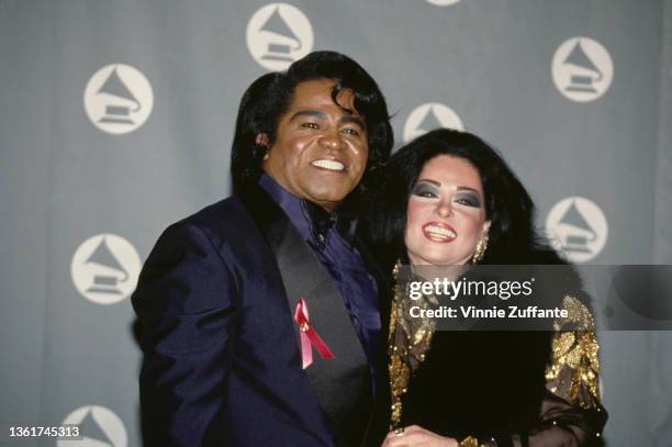 American singer and musician James Brown , wearing a blue tuxedo,and his wife, Adrienne Rodriguez , wearing a black-and-gold outfit, in the press...