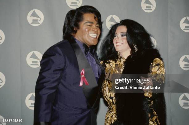 American singer and musician James Brown , wearing a blue tuxedo,and his wife, Adrienne Rodriguez , wearing a black-and-gold outfit, in the press...