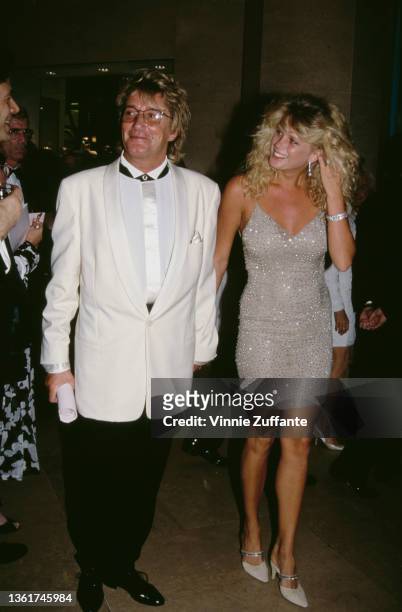 British singer and songwriter Rod Stewart, wearing a white tuxedo, and his wife, New Zealand model Rachel Hunter, wearing a sparkling minidress,...