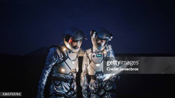 astronauts in futuristic suits looking for a route on new planet with illuminated tablet - wonderlust computer stock pictures, royalty-free photos & images