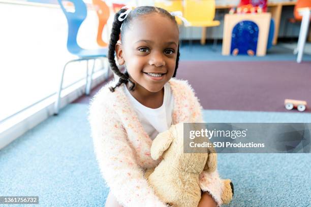 menina pré-escola fofa acaricia brinquedo recheado e sorrisos para a câmera - 4 5 anos - fotografias e filmes do acervo