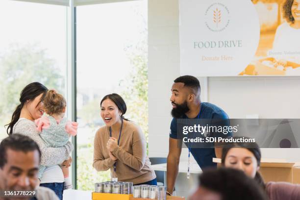 mid adult volunteers engage with baby in mother's arms - kids at community center stock pictures, royalty-free photos & images