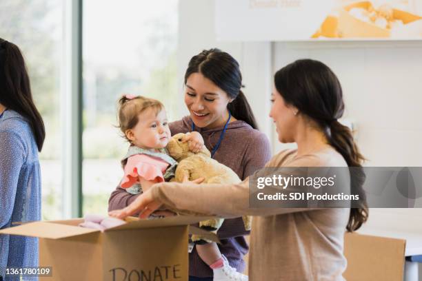 voluntária carrega bebê enquanto se voluntaria para unidade de roupas - toy drive - fotografias e filmes do acervo