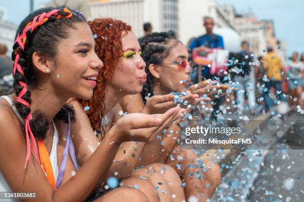 young women blowing confetti at street carnival party - plait stockfoto's en -beelden