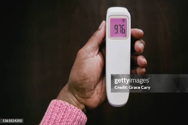 no fever: woman holds infrared thermometer displaying normal body temperature - digital thermometer stock pictures, royalty-free photos & images