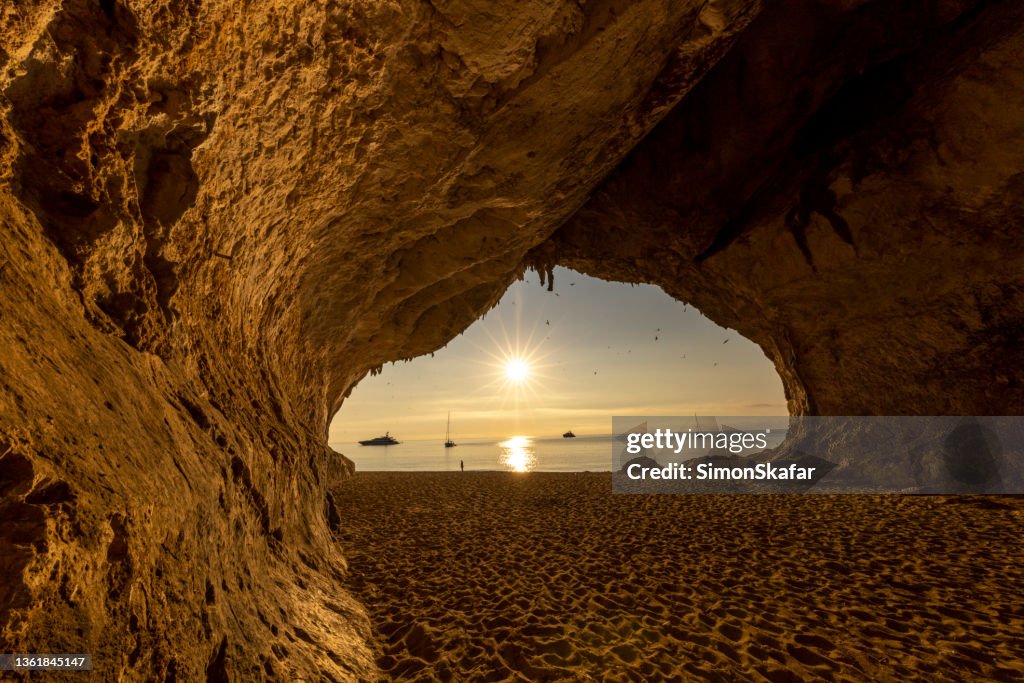 View of Cala Luna cave at sunset with sailing boats in background,Gulf of Orosei, Sardinia, Italy.