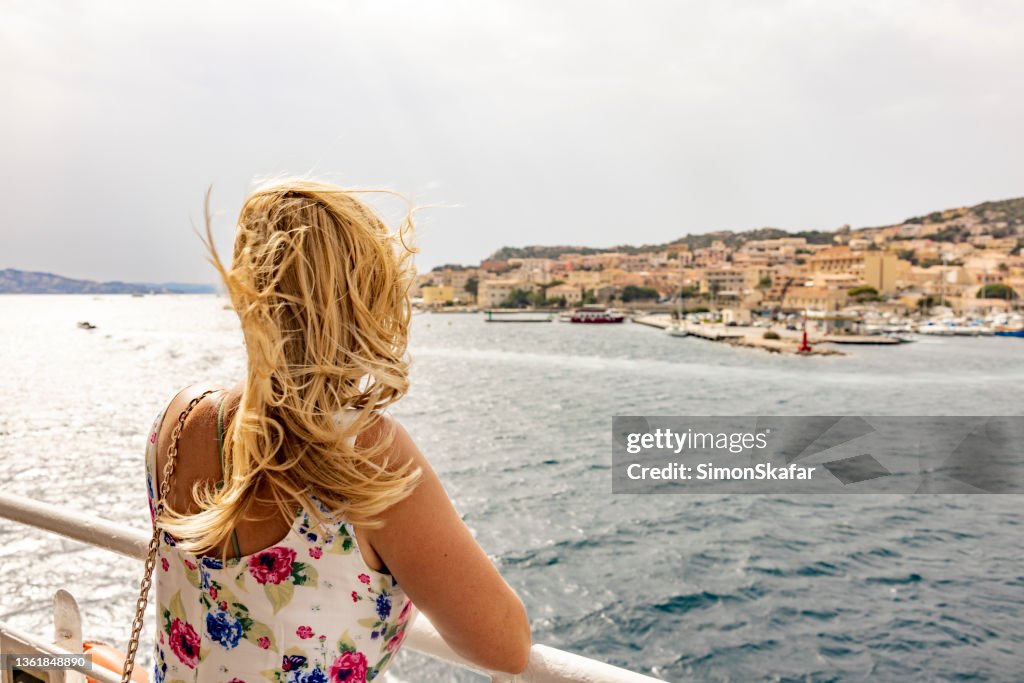 Blonde woman looking a small town from the cruise ship, Maddalena island, Sardinia, Italy.