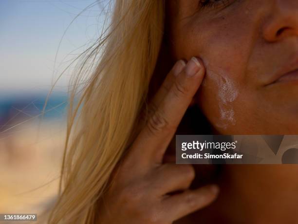 woman using suncream on the beach in summertime, sardinia, italy. - sun on face stock pictures, royalty-free photos & images