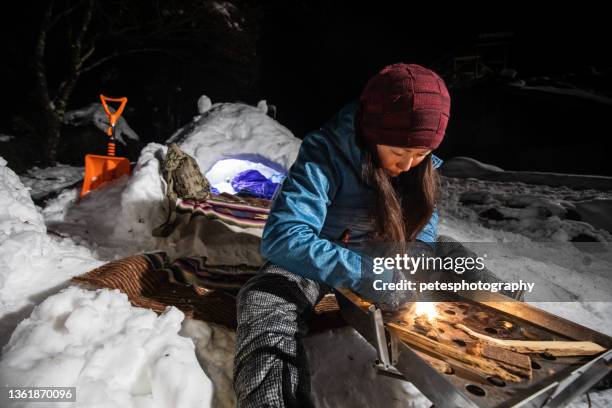 a woman starting campfire with ferro rod at snow camp - survivalist stock pictures, royalty-free photos & images