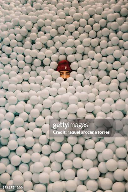 young adult man in a ball pit with a winter cap having fun - adult ball pit stock-fotos und bilder