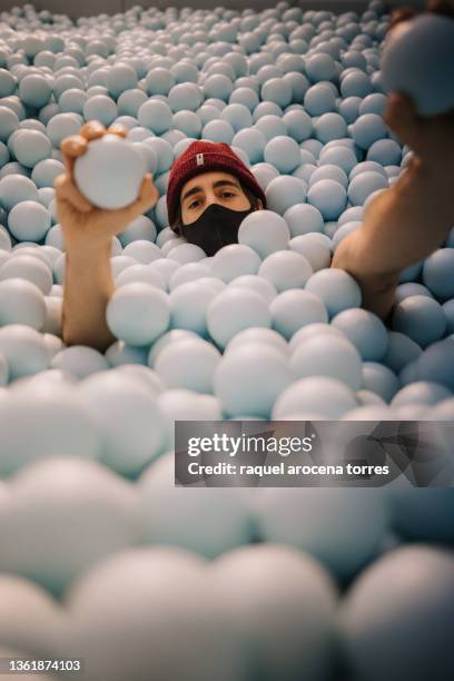 young adult man in a ball pit with a winter hat and mask having fun - adult ball pit stock pictures, royalty-free photos & images