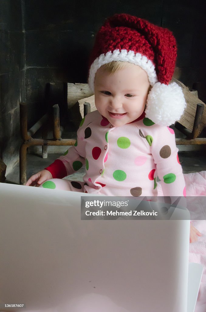Baby girl with Santa hat looking at laptop