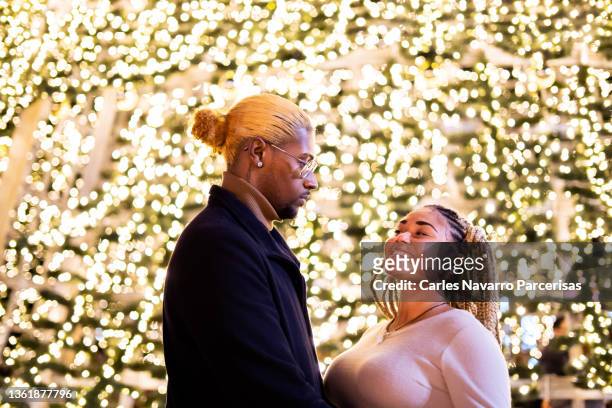 multiethnic couple standing next to a giant lit christmas tree - giant night of comedy stock-fotos und bilder