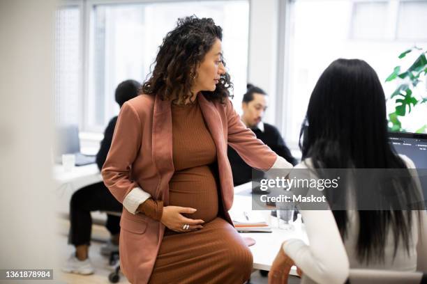 pregnant businesswoman discussing with female colleague over computer in office - working mom stock pictures, royalty-free photos & images