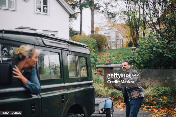 man guiding female friend to reverse sports utility vehicle behind at driveway - reversing stock pictures, royalty-free photos & images