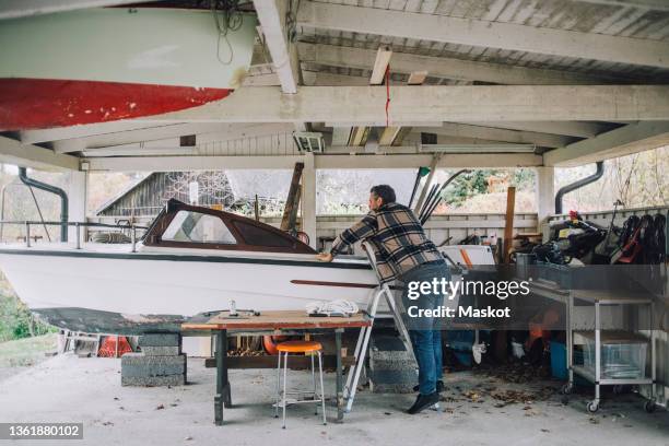 mature man repairing speedboat in garage - repairing boat stock pictures, royalty-free photos & images