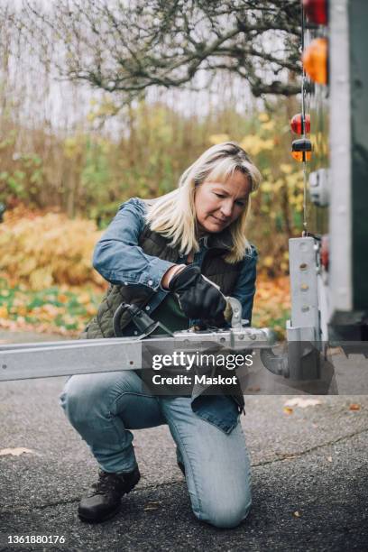 mature woman fastening trailer to sports utility vehicle on driveway - one woman only kneeling stock pictures, royalty-free photos & images