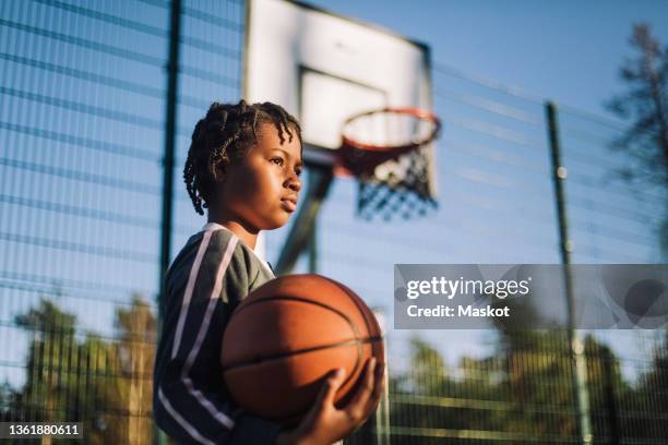 contemplative girl looking away with basketball on sunny day - basketball stockfoto's en -beelden