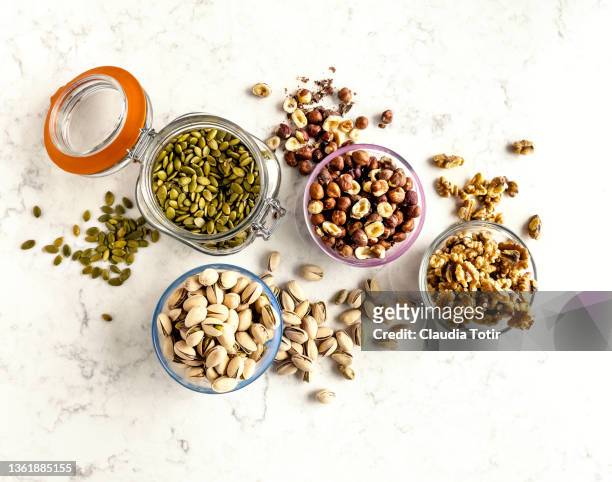 bowls and jars with seeds and nuts (pistachios, walnuts, hazelnuts, and pumpkin seeds) on white background - pflanzensamen stock-fotos und bilder