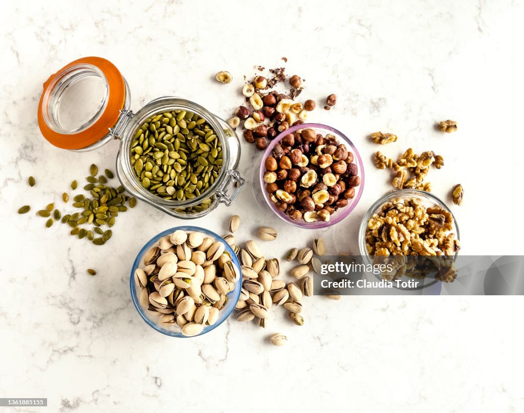 Bowls and jars with seeds and nuts (pistachios, walnuts, hazelnuts, and pumpkin seeds) on white background