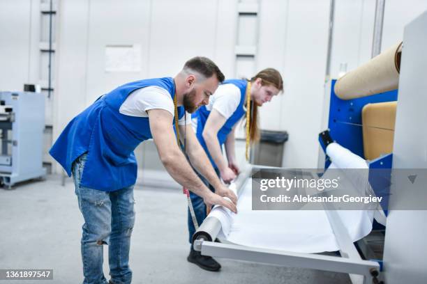 due operai maschi di una fabbrica tessile che mostrano il lavoro di squadra mentre arrotolano la stoffa - textile printing foto e immagini stock