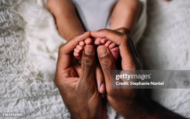 father hand with baby feet - cute black newborn babies stock-fotos und bilder