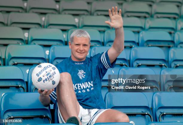 Smiling and waving Paul Gascoigne wearing the Rangers adidas home shirt holds aloft a Sondico matchball after completing his transfer from Lazio of...