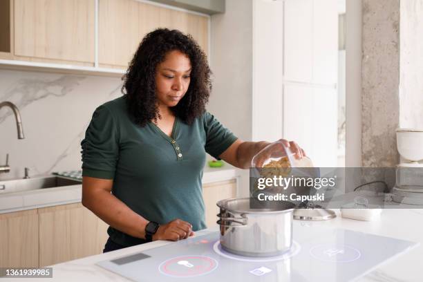 donna che mette la pasta a cuocere in acqua bollente su un piano cottura a induzione intelligente - woman cook foto e immagini stock