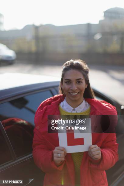 portrait happy young woman holding learner permit next to car - learner driver stock-fotos und bilder