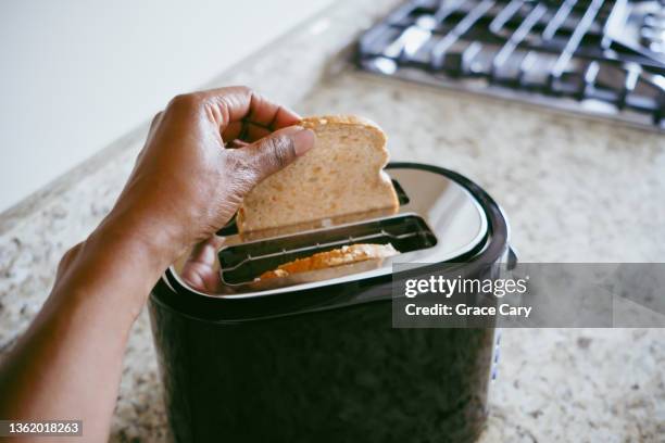 woman puts bread into toaster - carbohidrato fotografías e imágenes de stock