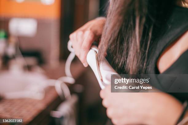 woman using hair straightener in the domestic bathroom - hair styling photos et images de collection