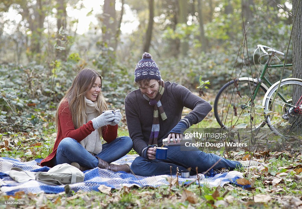 Man and woman with flask of tea in Autumn setting.
